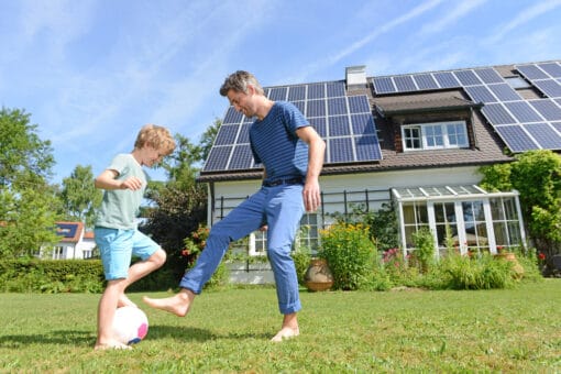otec a syn si hrají před rodinným domem s fotovoltaikou