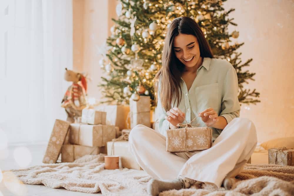 Mladá žena pod stromečkem balí dárek, který koupila díky půjčce na Vánoce